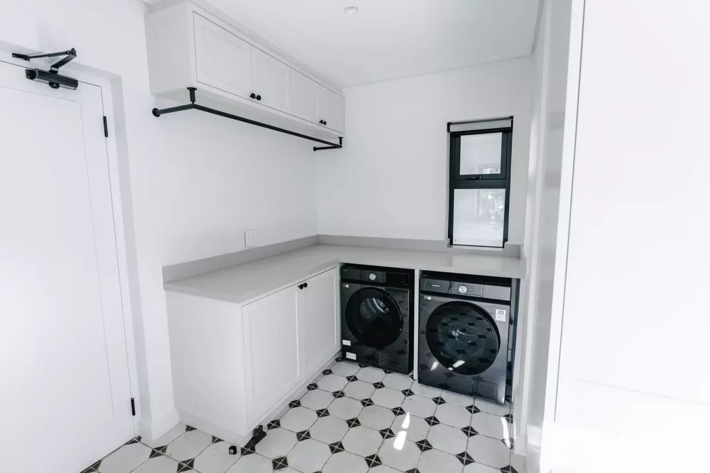 Laundry room with white cabinets, grey countertop, and black appliances.