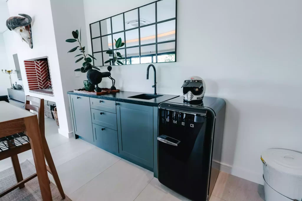 Kitchenette with dark green cabinetry, black countertop, and a black Smeg refrigerator.