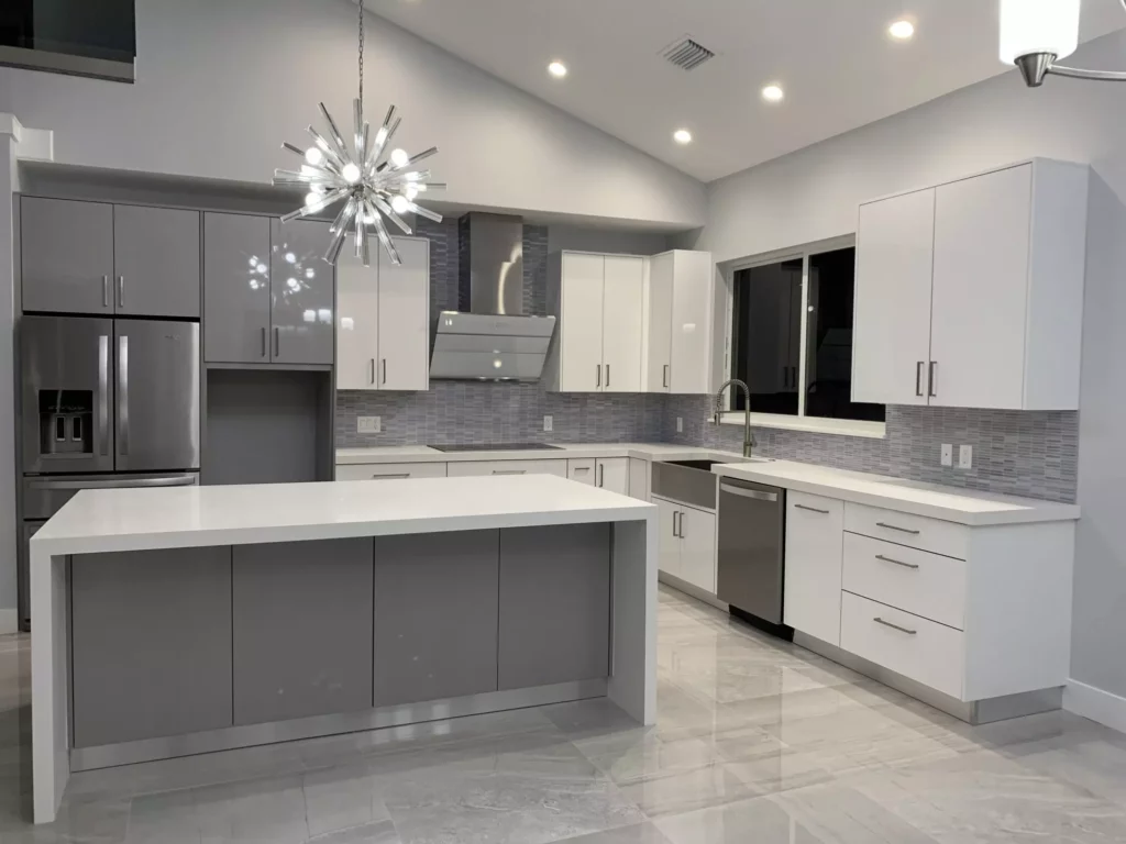 Modern kitchen featuring a large grey center island with a white waterfall countertop, mixed white and grey high-gloss cabinets, stainless steel appliances, and a striking starburst pendant light.
