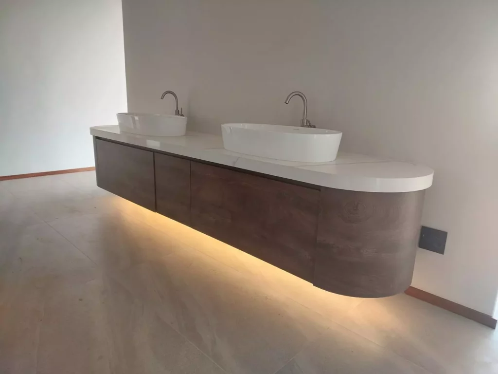 Modern floating bathroom vanity with dark wood cabinets, a curved edge, a white marble countertop, double vessel sinks, and under-cabinet LED strip lighting.