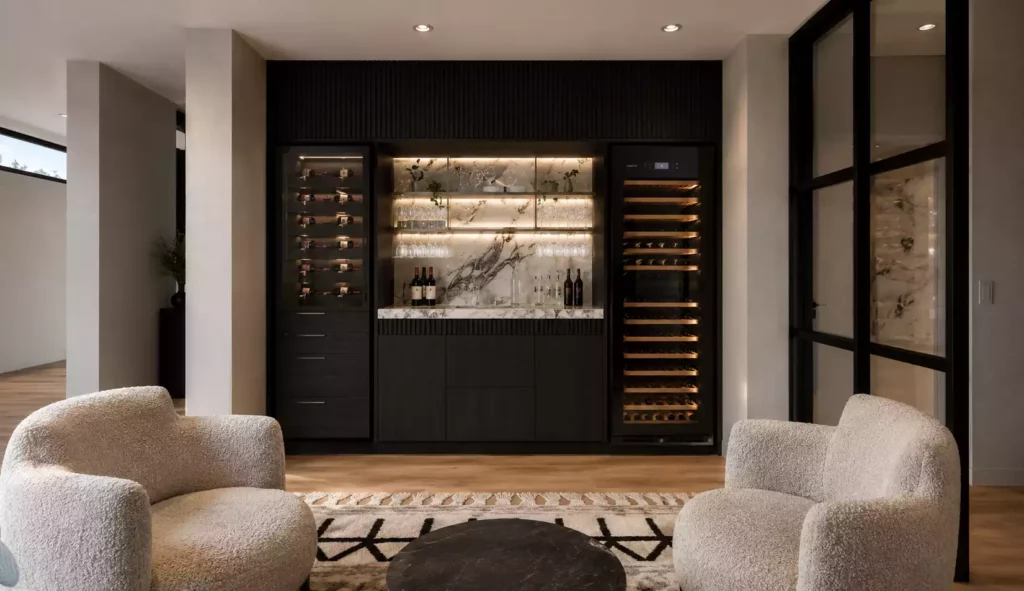 Modern black home bar with a marble countertop, built-in cabinets, and two cream bouclé armchairs.