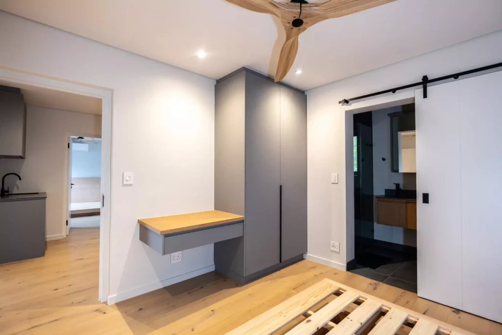 Bedroom featuring a grey wardrobe with an integrated desk, a wooden bed frame, and a sliding barn door leading to an en-suite bathroom.