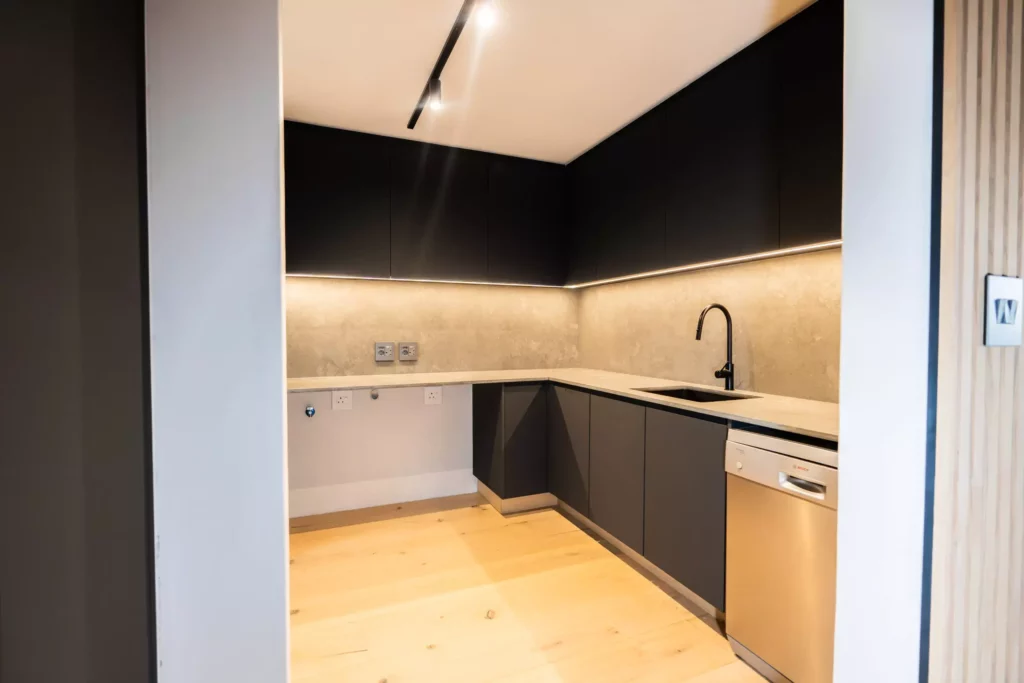 Scullery with dark matte cabinetry, light grey countertops, and a dishwasher.
