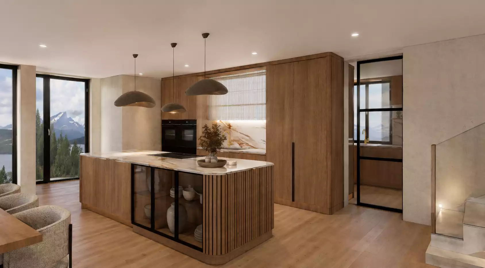 A modern, luxury kitchen featuring extensive warm wood cabinetry, a large kitchen island with a marble countertop, an integrated glass-fronted display section, and wood-slat detailing. The space is accented by three distinctive pendant lights, views of mountainous terrain through large windows, and a doorway with black framing leading to a staircase.