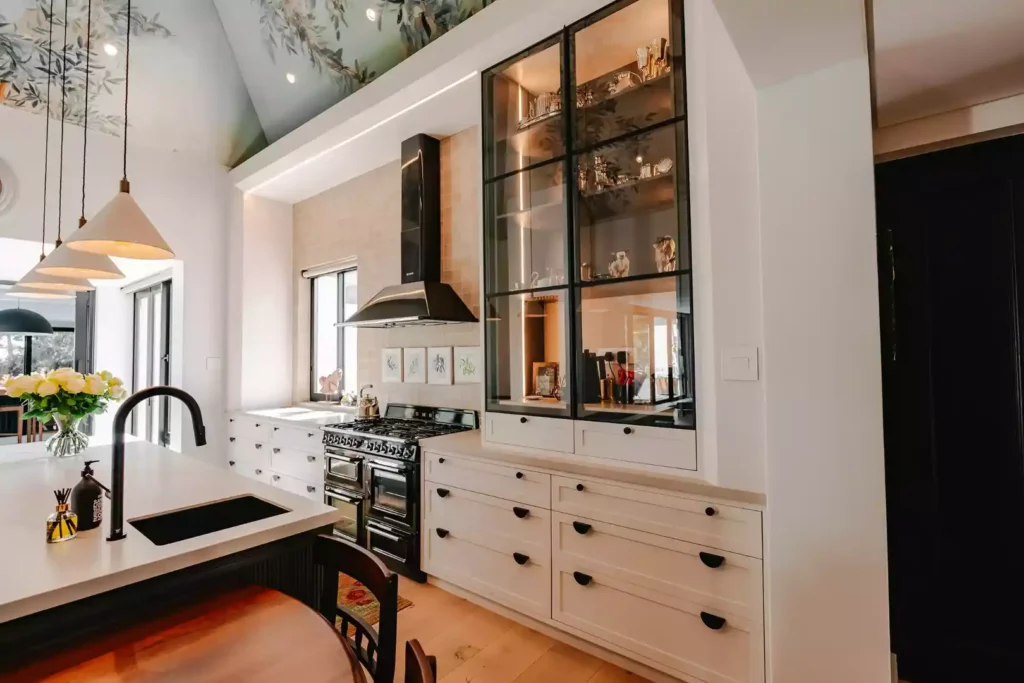 Modern kitchen with white cabinetry, black range cooker, and tall glass display cabinet.