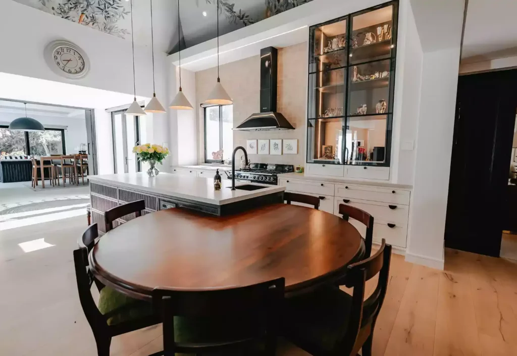 Modern kitchen with a large circular dining table, white island, and a tall glass display cabinet.