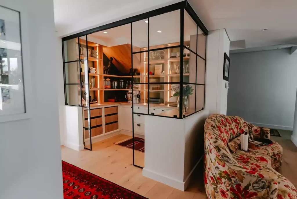 Walk-in pantry enclosed by a black-framed glass wall.
