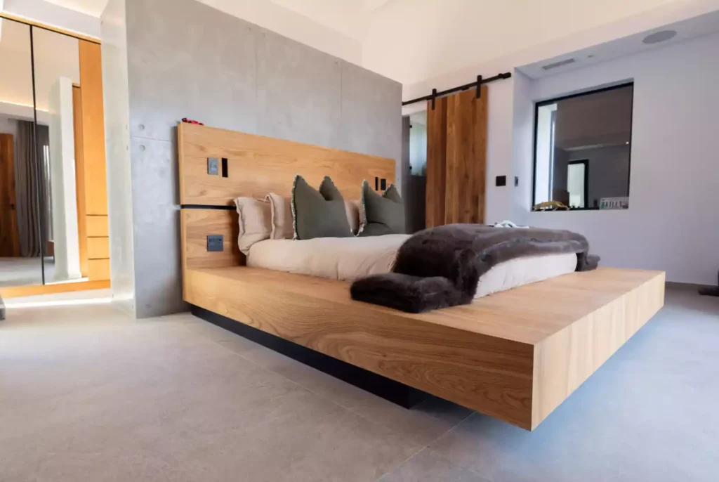 A modern bedroom featuring a custom floating wooden platform bed with a matching high headboard against a concrete accent wall.