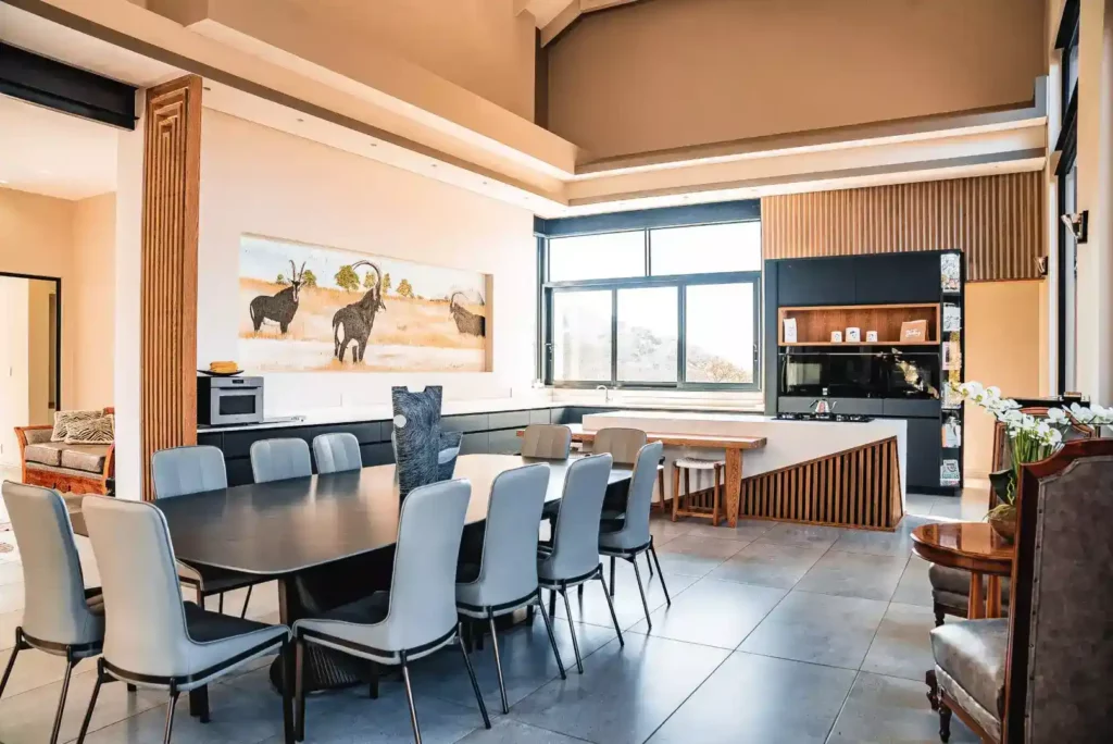 Open-plan dining and kitchen area with a long black table, modern chairs, and a mural on the wall.