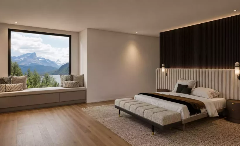 A tranquil bedroom featuring a large window with a built-in bench seat offering views of mountains and water. The room includes a bed with a tall, light-textured headboard against a dark wood-slat accent wall, paired with a matching bench at the foot of the bed and minimalist bedside tables.